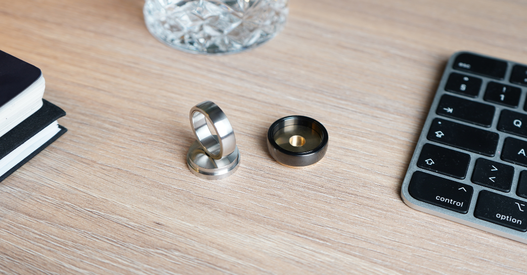 A steel and a black Polar Ring sitting on steel and gold desk stands.